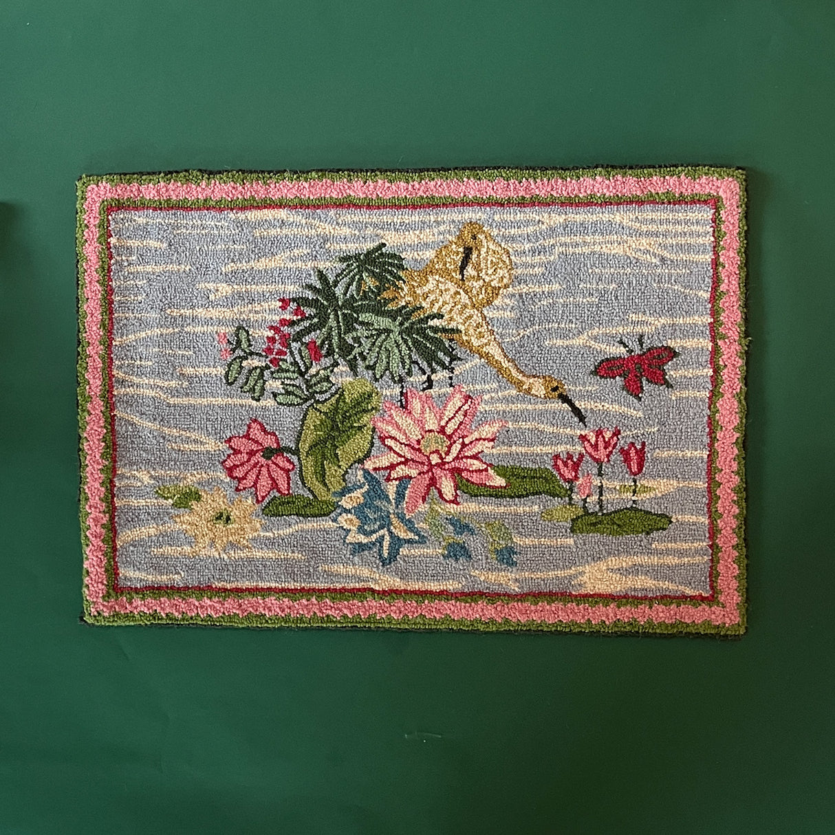 A small pink green and blue rug featuring waterlillies and heron motifs. 