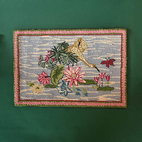 A small pink green and blue rug featuring waterlillies and heron motifs. 