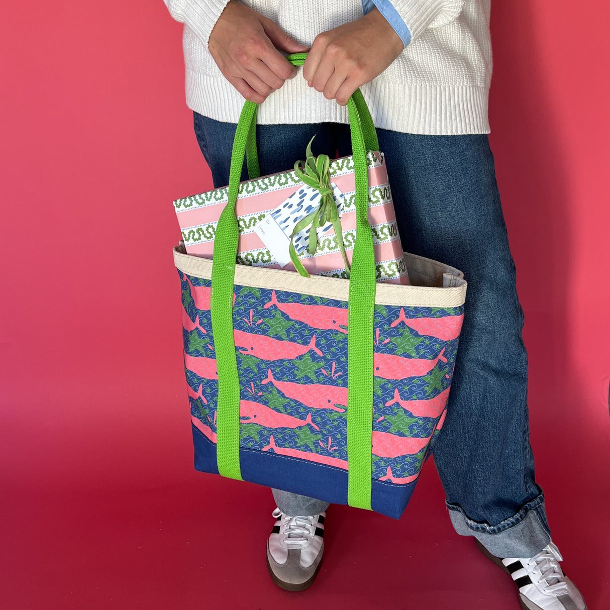 Whale of a Time canvas tote bag with lime straps and blue fabric with a repeating pink whale  and green star motif with presents and being held by model.