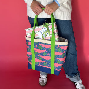 Whale of a Time canvas tote bag with lime straps and blue fabric with a repeating pink whale  and green star motif with presents and being held by model.