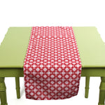 Monserrat Lacquer Red is a no-iron cloth table runner with a geometric pattern, displayed on a green table.