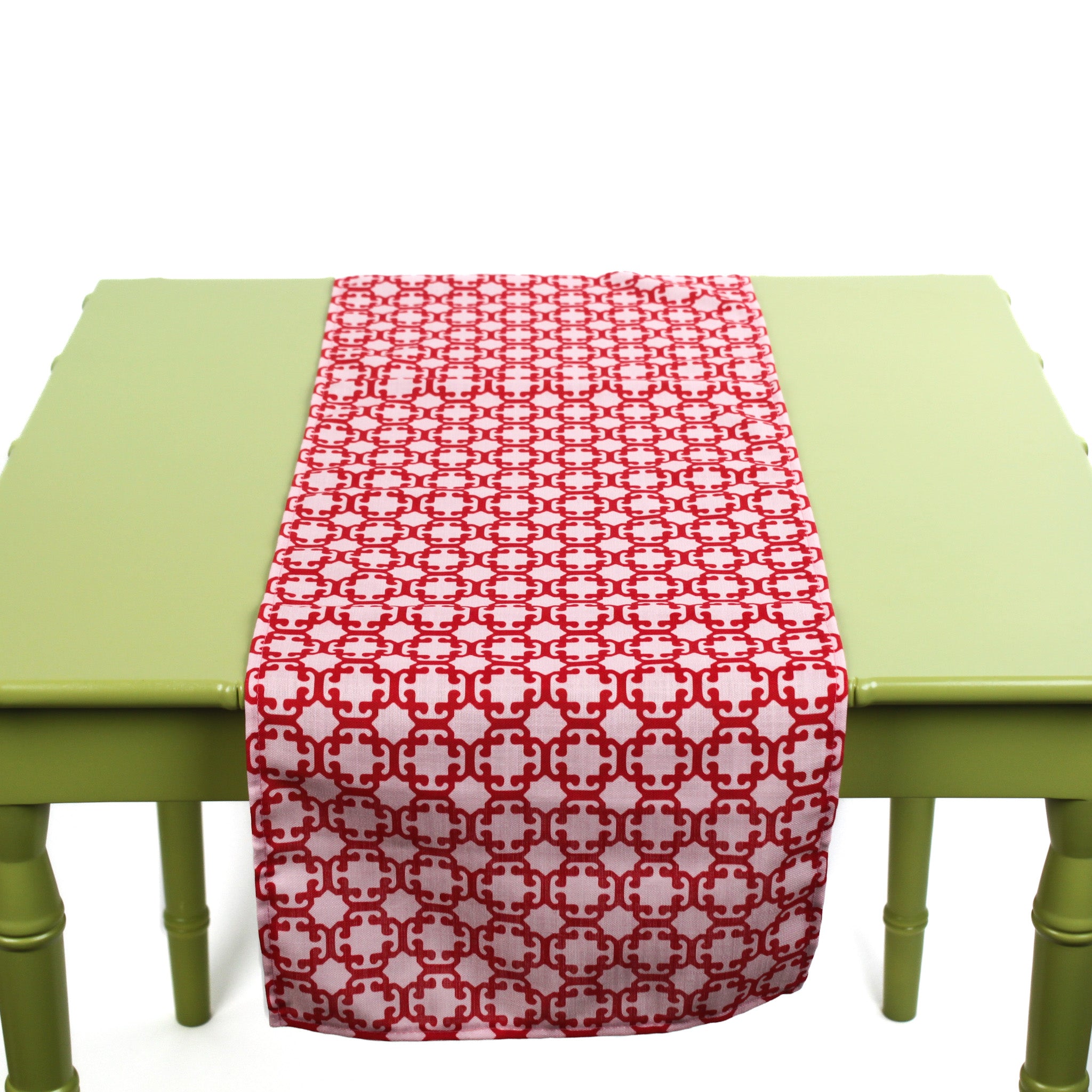 Monserrat Lacquer Red is a no-iron cloth table runner with a geometric pattern, displayed on a green table.