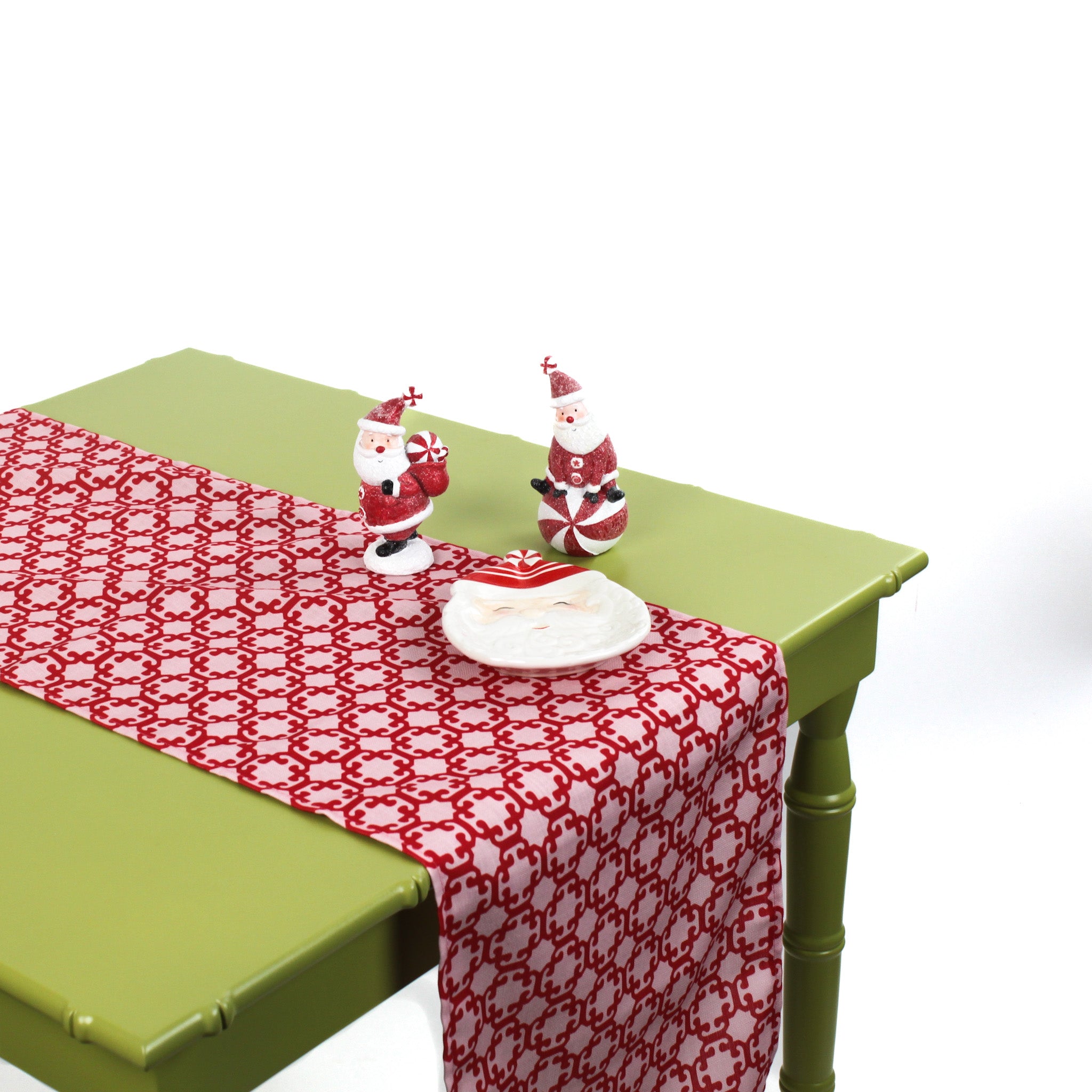 Monserrat Lacquer Red is a no-iron cloth table runner with a geometric pattern, displayed on a table with some ceramic christmas dinnerware