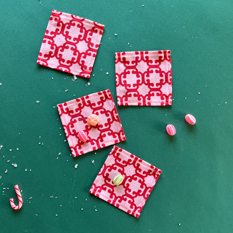 A set of four Monserrat lacquer red cloth cocktail napkins on a green background with candies scattered about