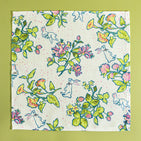 A multicolor bunny and strawberry print fabric Easter napkin against a green background. 