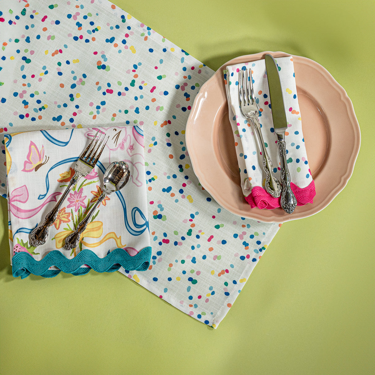 A Springtime confetti print cloth table runner with a pink plate and napkin on top with cutlery