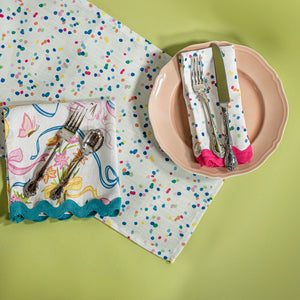A Springtime confetti print cloth table runner with a pink plate and napkin on top with cutlery