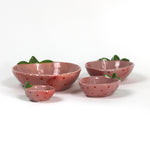 a set of four pink ceramic strawberry dishes in graduating sizes.