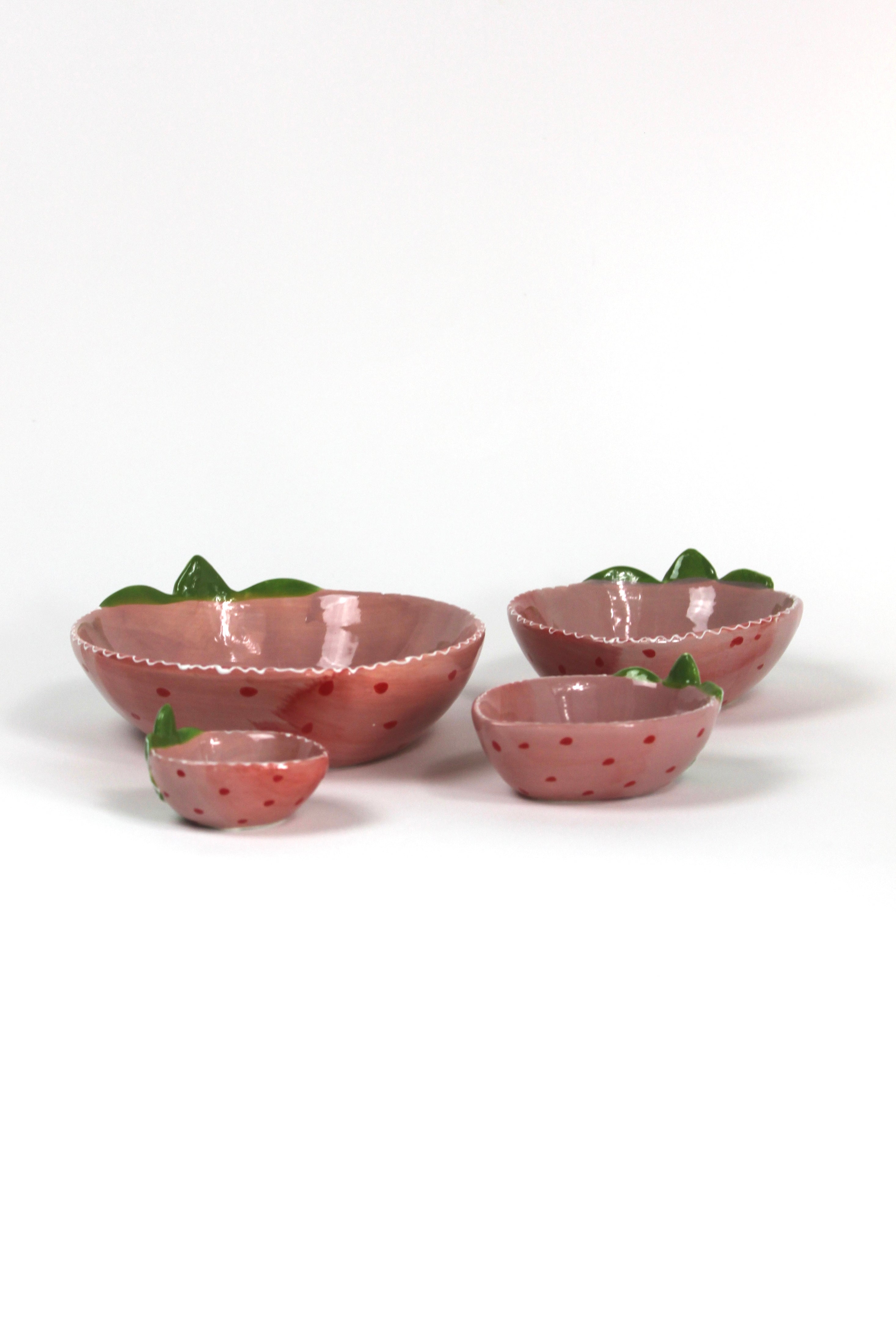 a set of four pink ceramic strawberry dishes in graduating sizes.