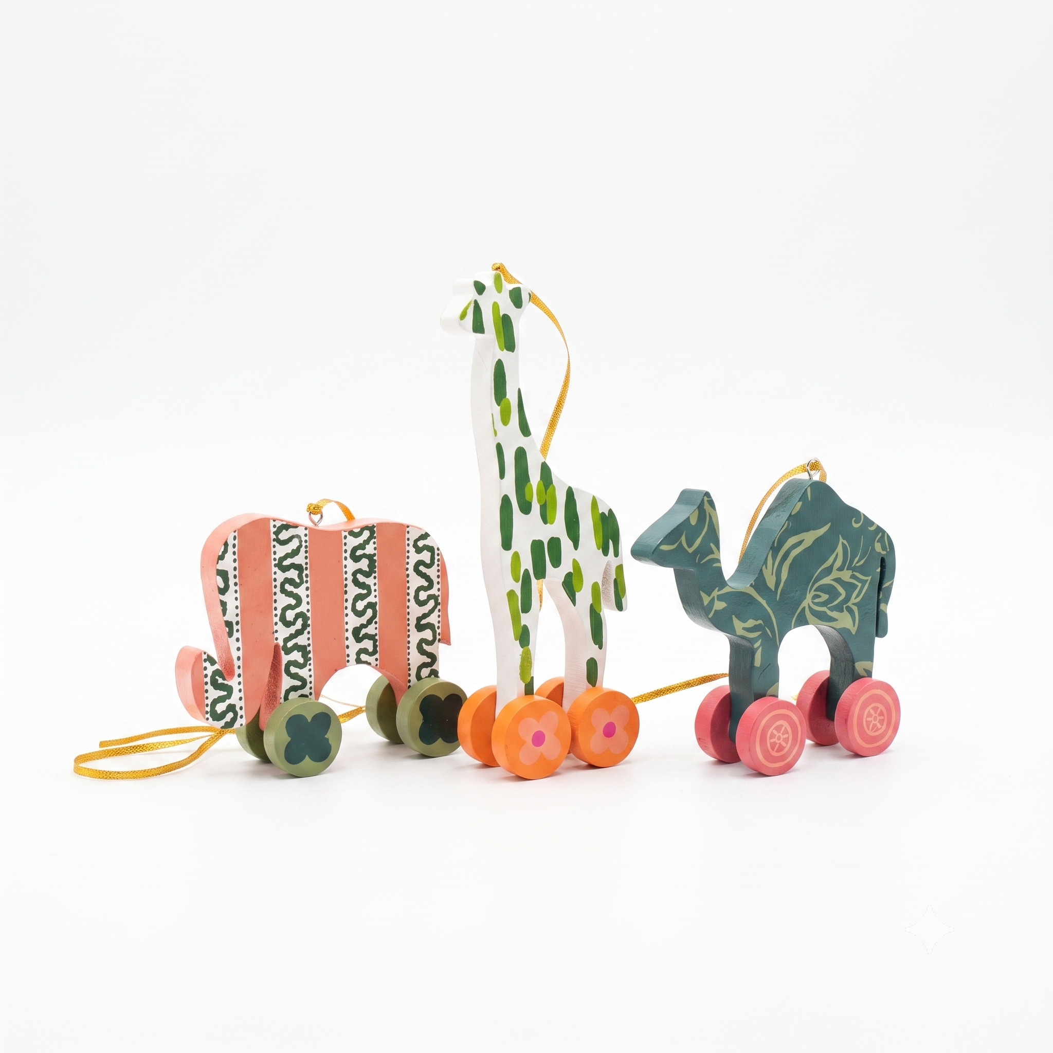 Three hand-painted wooden animal toys with wheels on a clean white background: a pink and green patterned elephant, a white giraffe with green spots, and a teal camel with gold leaf patterns.