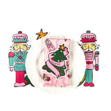 Christmas tabletop entertaining display featuring nutcracker cutout decorations, a white ruffled plate, and a pink holiday napkin with personalized Christmas tree design, arranged on a white background.