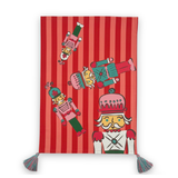 A rectangular red and pink striped tea towel, decorated with cartoon nutcracker illustrations and finished with two tassel ties at the bottom corners.