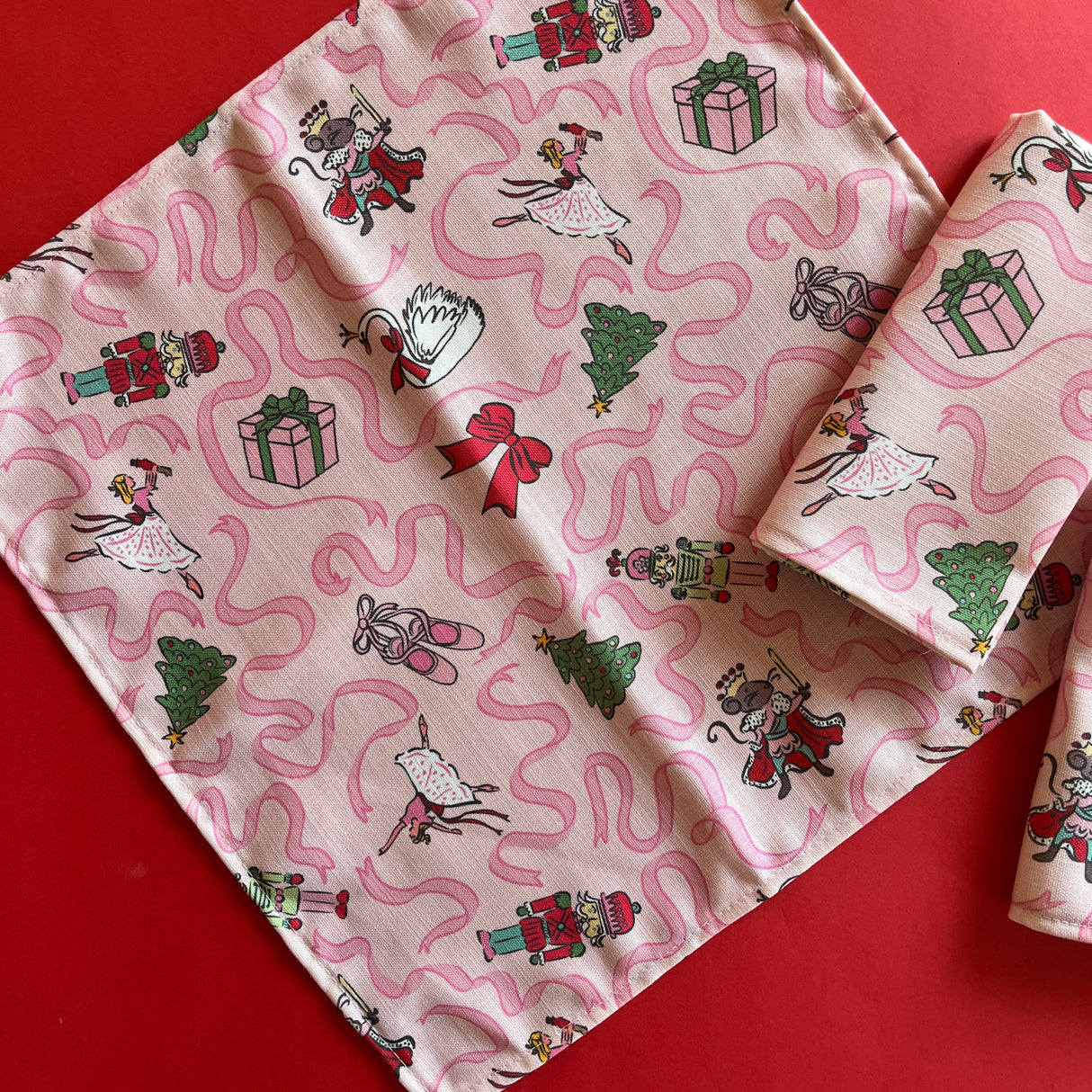 Open view of Nutcracker ballet characters on a light pink napkin with darker pink ribbons.