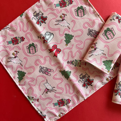 Open view of Nutcracker ballet characters on a light pink napkin with darker pink ribbons.