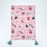 Pink Christmas tea towel featuring Nutcracker-themed illustrations with ribbons, ballerinas, swans, Christmas trees, and presents, finished with teal tassels on each corner.