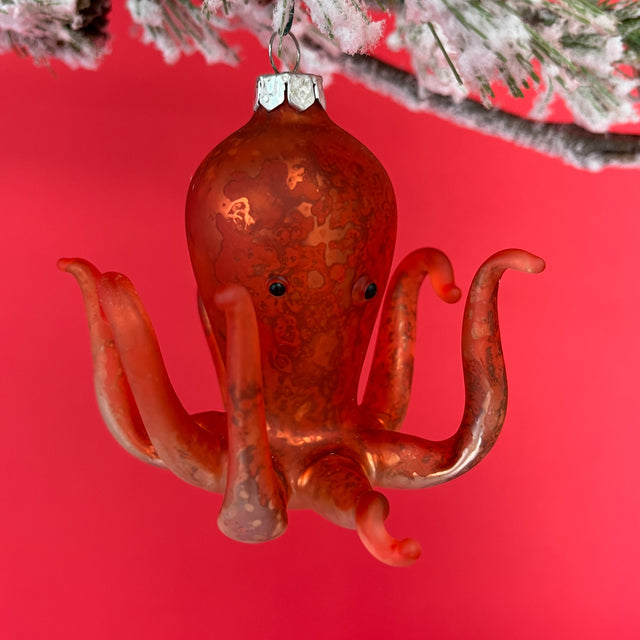 An orange glass octopus christmas ornament hanging against a red background