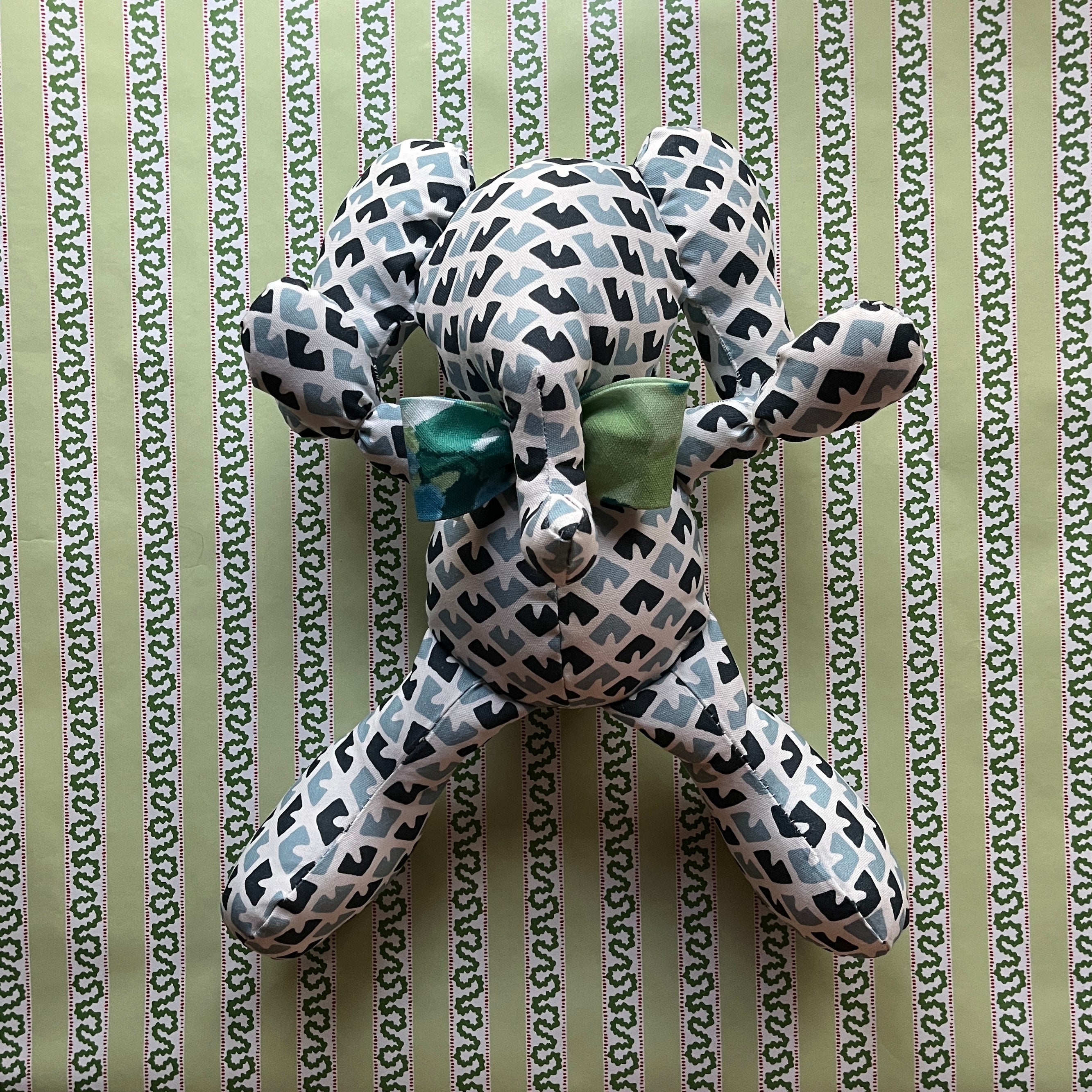 Blue and white patterned stuffed elephant toy with a green bow.