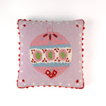 Pink Christmas pillow with an ornament design on a light pink background and red pom pom trim