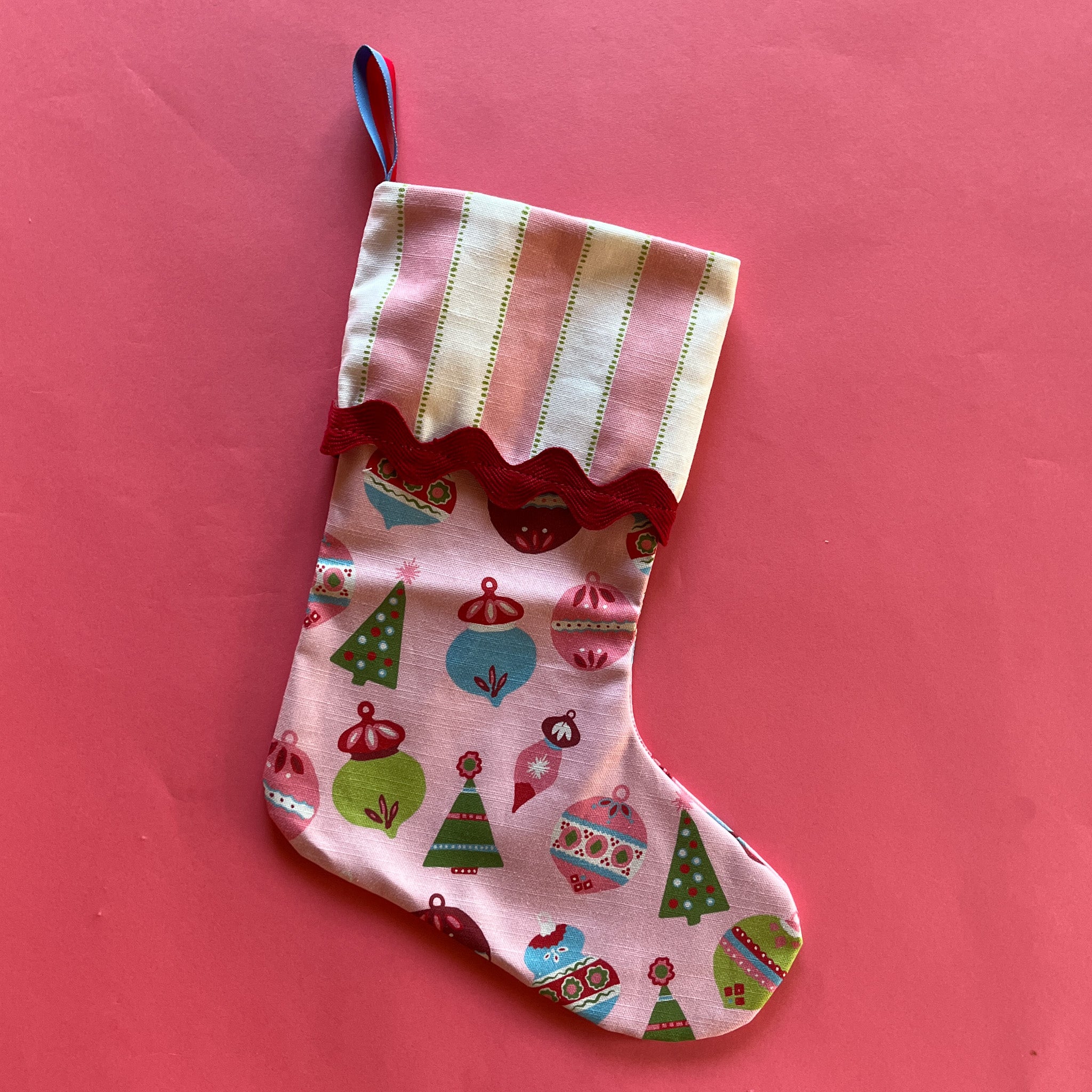 An ornament print pink Christmas stocking with a folded striped top