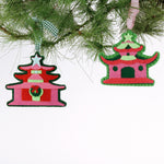 Two red and green pagoda-shaped Christmas ornaments hanging on a tree branch.