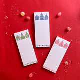 a set of 3 Pagodas Skinny Notepad in pink, blue and green, featuring illustrated pagoda designs and floral border. they are placed in a red surface with some candies scattered