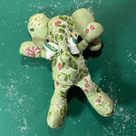 Green floral patterned stuffed elephant toy with a white and green bow in a green background.