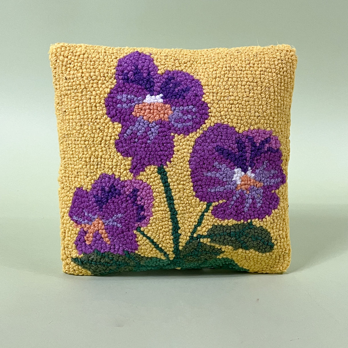 A spring pillow with purple pansies on a yellow background. 