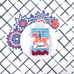 A patriotic table setting featuring a horse themed place card, red white and blue star placemat, white dinner plate, and blue patterned napkin.