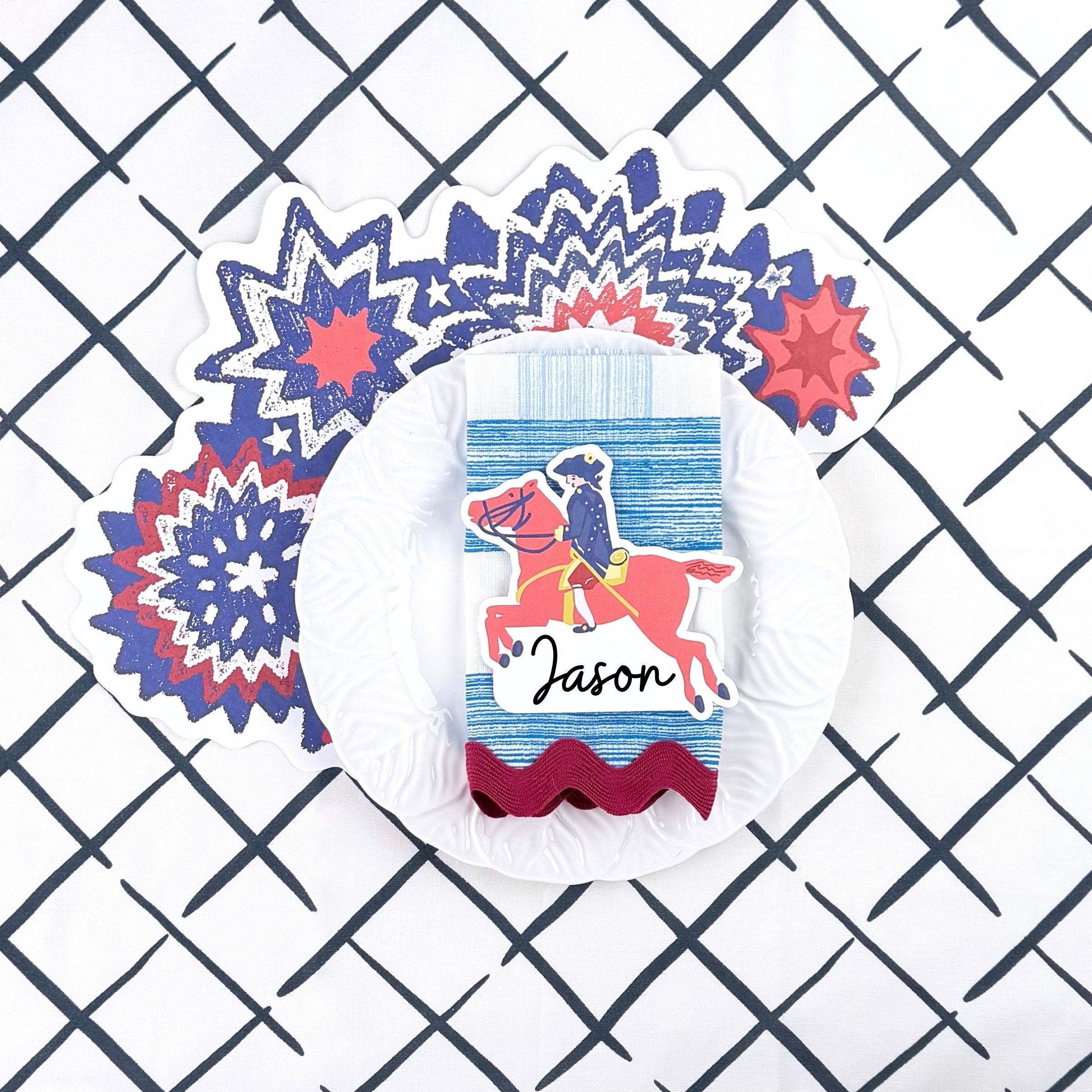 A patriotic table setting featuring a horse themed place card, red white and blue star placemat, white dinner plate, and blue patterned napkin.