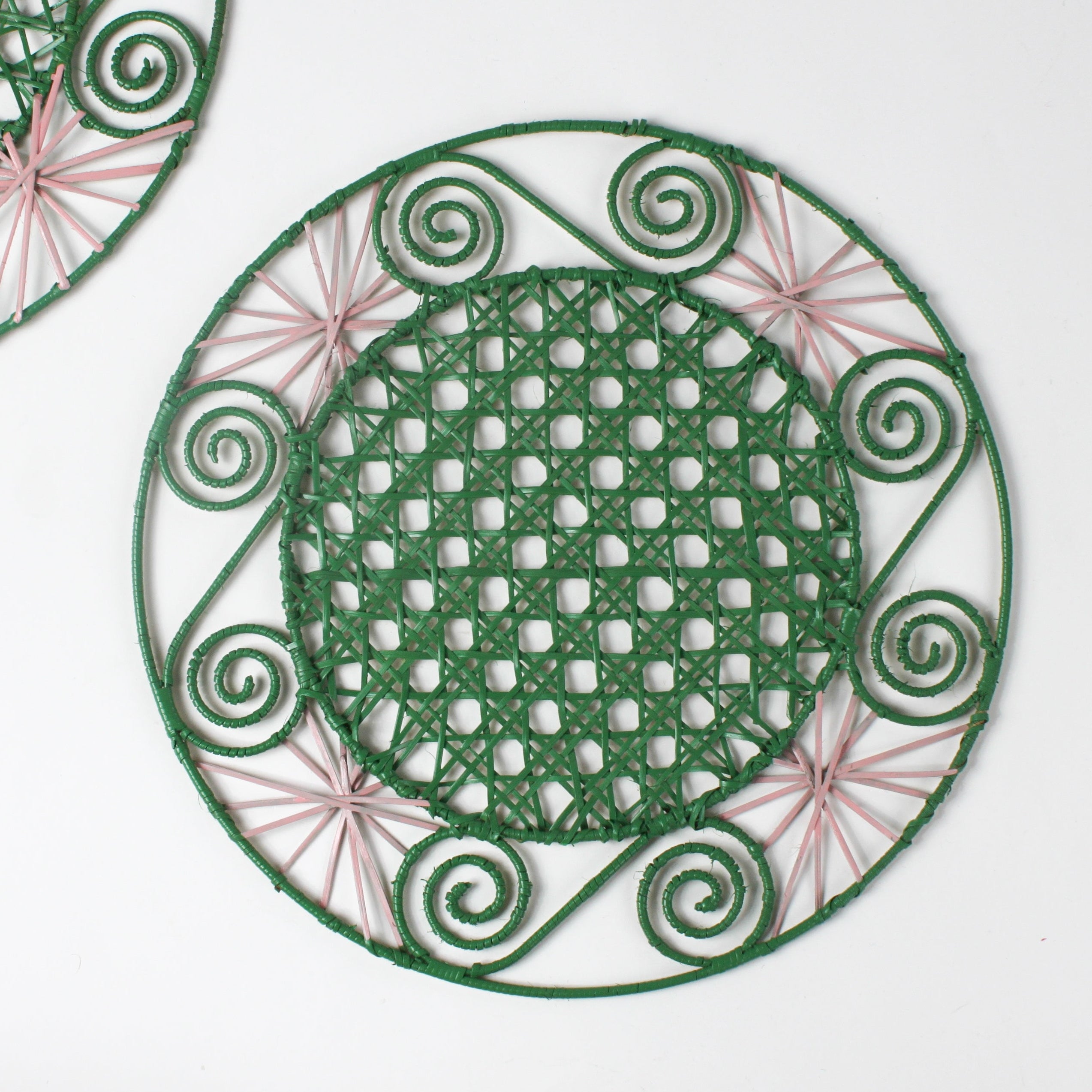 a pink and green round rattan placemat with green swirls and pink star woven motifs against a white backround.