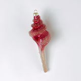Decorative pink glass Christmas ornament shaped like a conch shell on a white background
