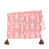 a pink chinoiserie tea towel with white pagodas and green and pink tassels in the corner resting on a white background. 