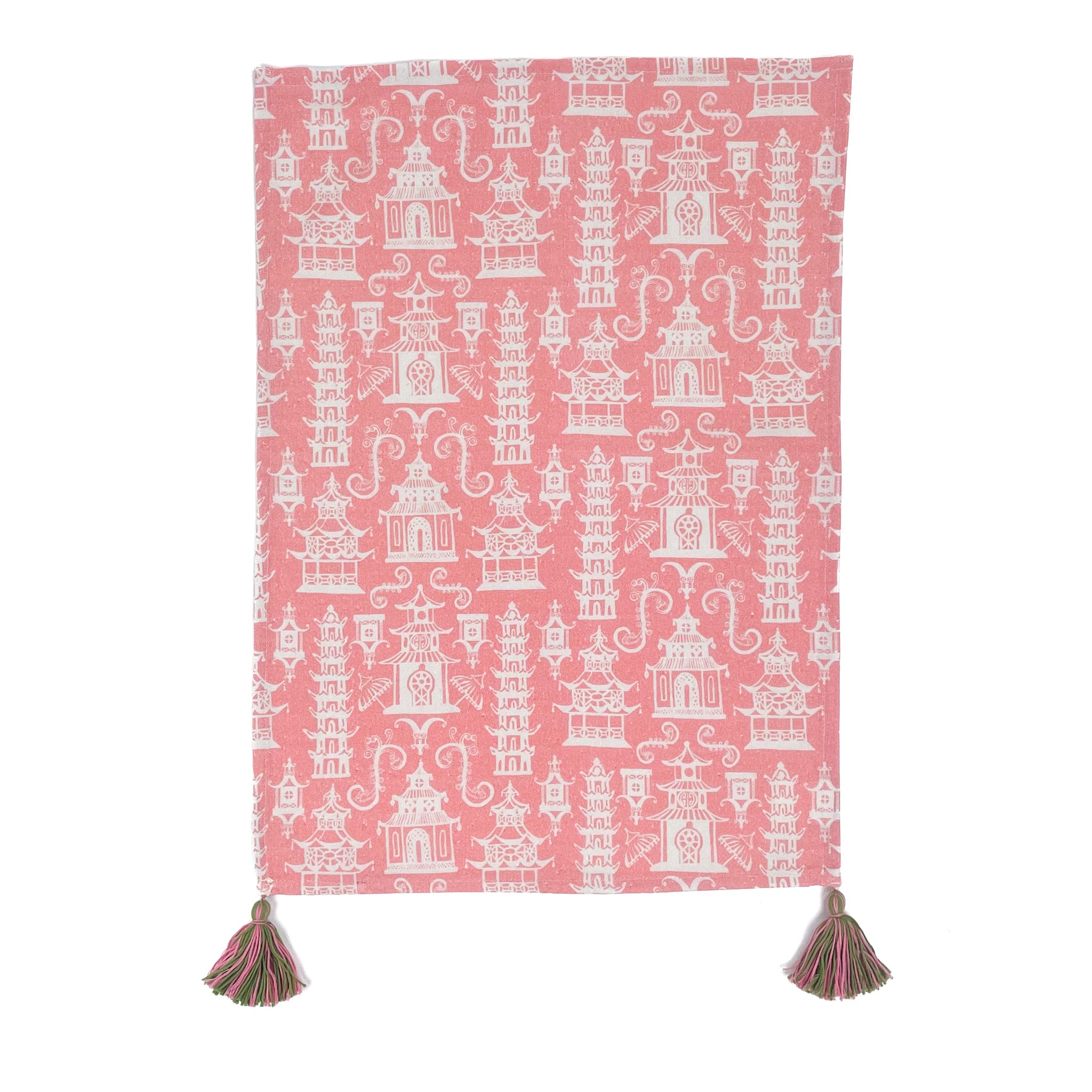 a pink chinoiserie tea towel with white pagodas and green and pink tassels in the corner resting on a white background. 