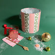 Pink and green striped ice bucket surrounded by a cockail glass, napkin and ornaments.