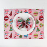 a red candy cane christmas napkin ring filled with a pink christmas napkin with white plate and ornament napkin against a white background. 