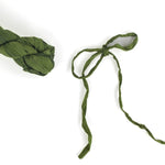 a recycled torn-silk ribbon in green laid in a white surface, with a ribbon tied sample
