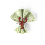 Red lobster napkin ring displayed on a green patterned cloth napkin.