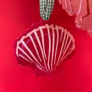 Red felt christmas ornament in the shape of a scallop shell with a green gingham ribbon against a red background