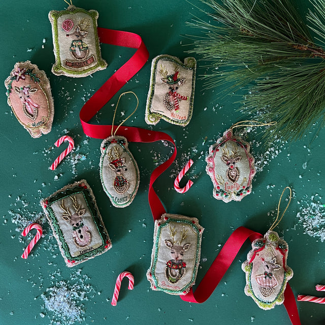 Set of 8 fabric christmas tree ornaments with different reindeer motifs embroidered on to each one sitting against a green background sprinkled with snow and mini candy canes