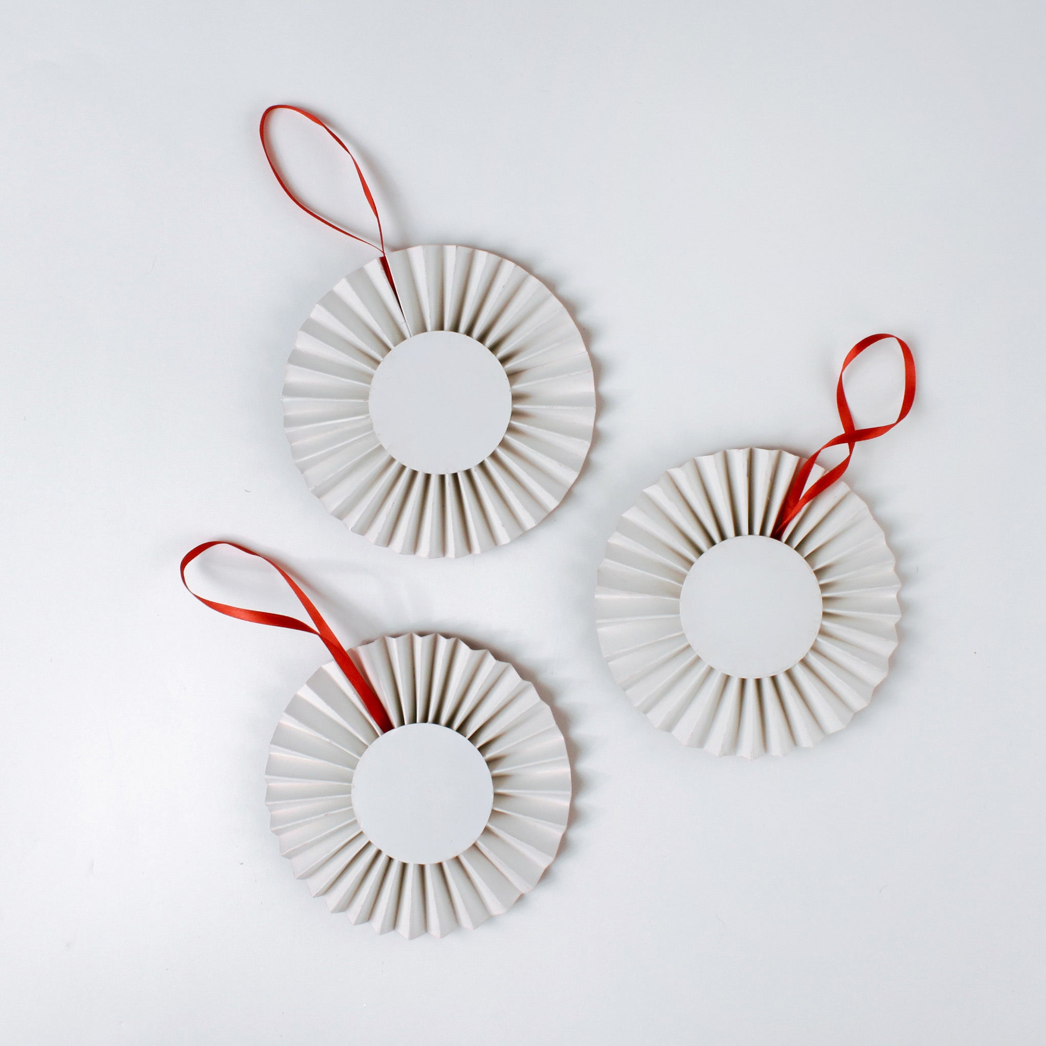 back of three retro-style ruffled paper Christmas ornaments featuring vintage illustrations of a reindeer, Santa in his sleigh, and a snowman, accented with red pleated borders and hanging ribbons