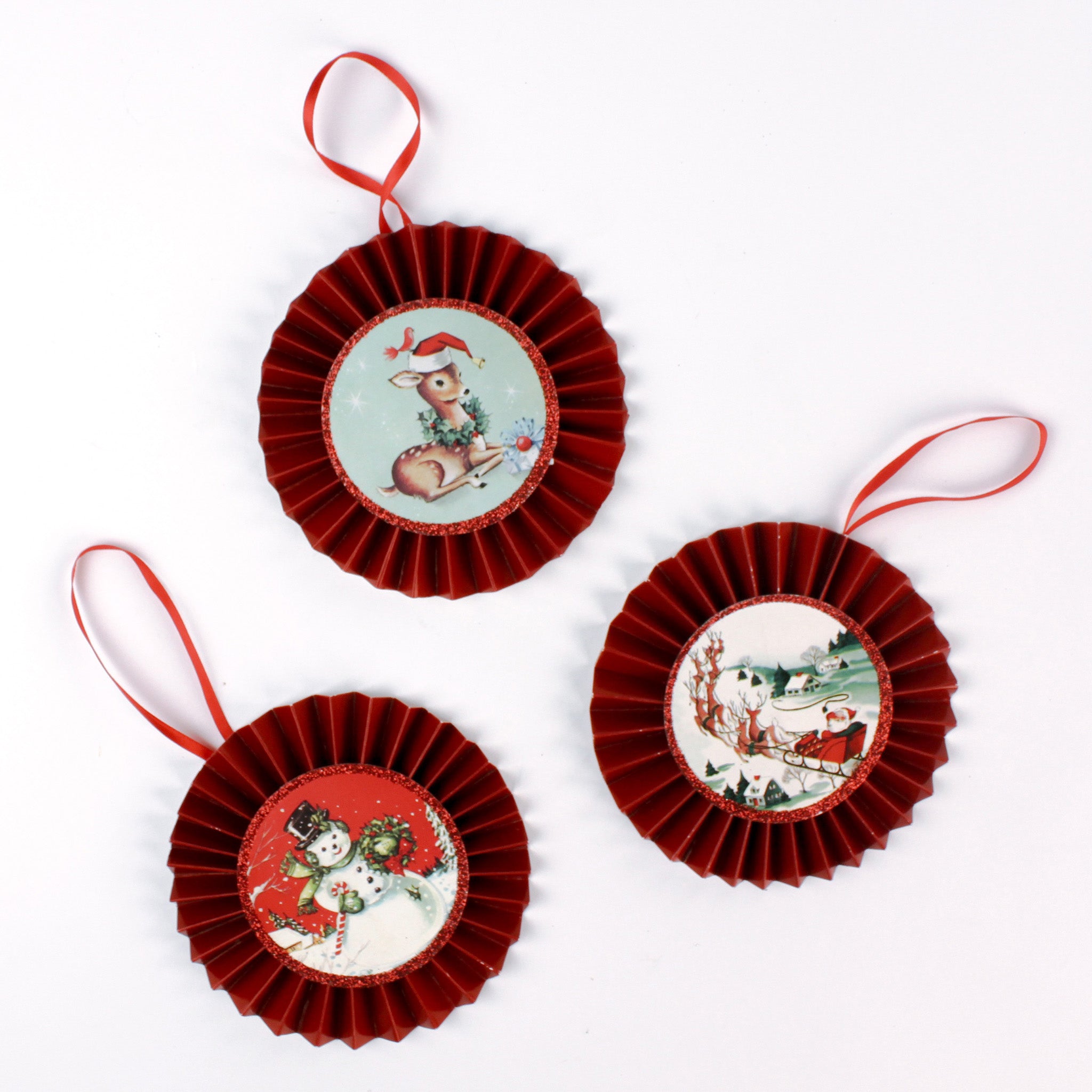 Set of three retro-style ruffled paper Christmas ornaments featuring vintage illustrations of a reindeer, Santa in his sleigh, and a snowman, accented with red pleated borders and hanging ribbons