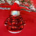 the reverse side of a glass snowman ornament wearing a red jacket and hat hanging from a christmas tree branch against a red background. 