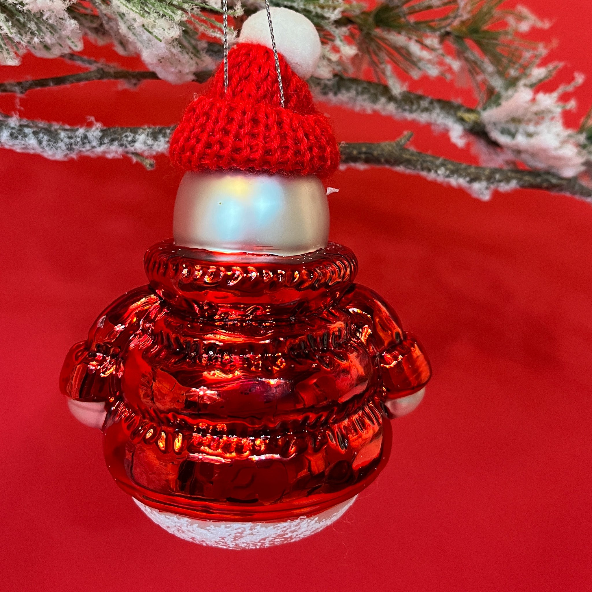 the reverse side of a glass snowman ornament wearing a red jacket and hat hanging from a christmas tree branch against a red background. 