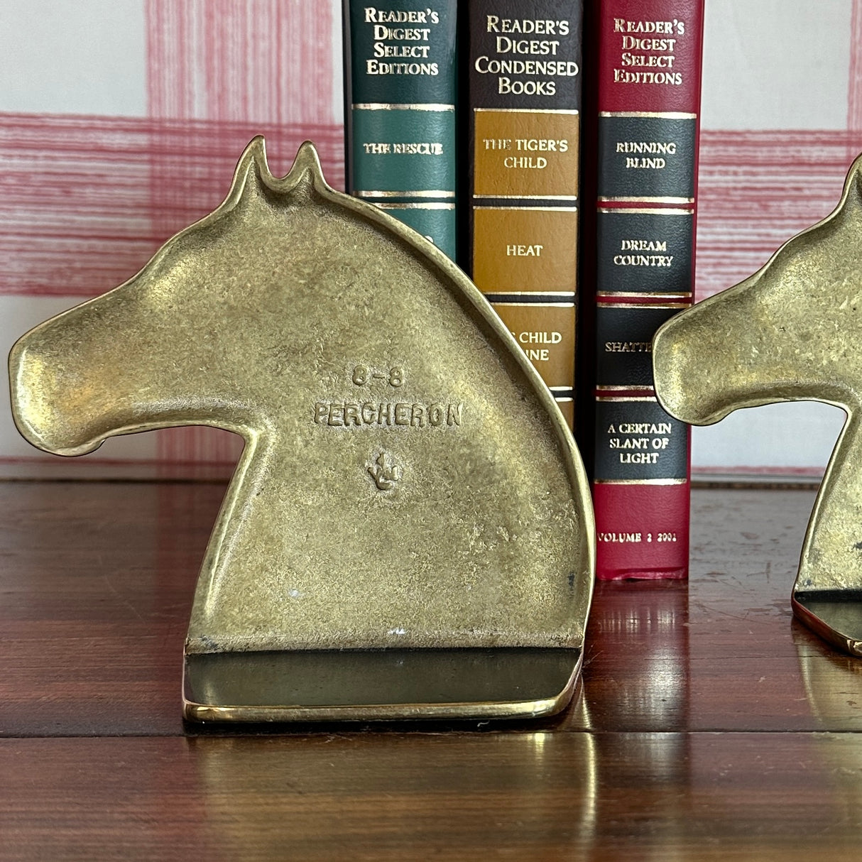 The reverse side of two brass horse bookends with some books in the background. 