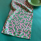 Pink ribbons swirl around on a green background in Madcap Cottage's Ribbons Pink and Green cloth table runner