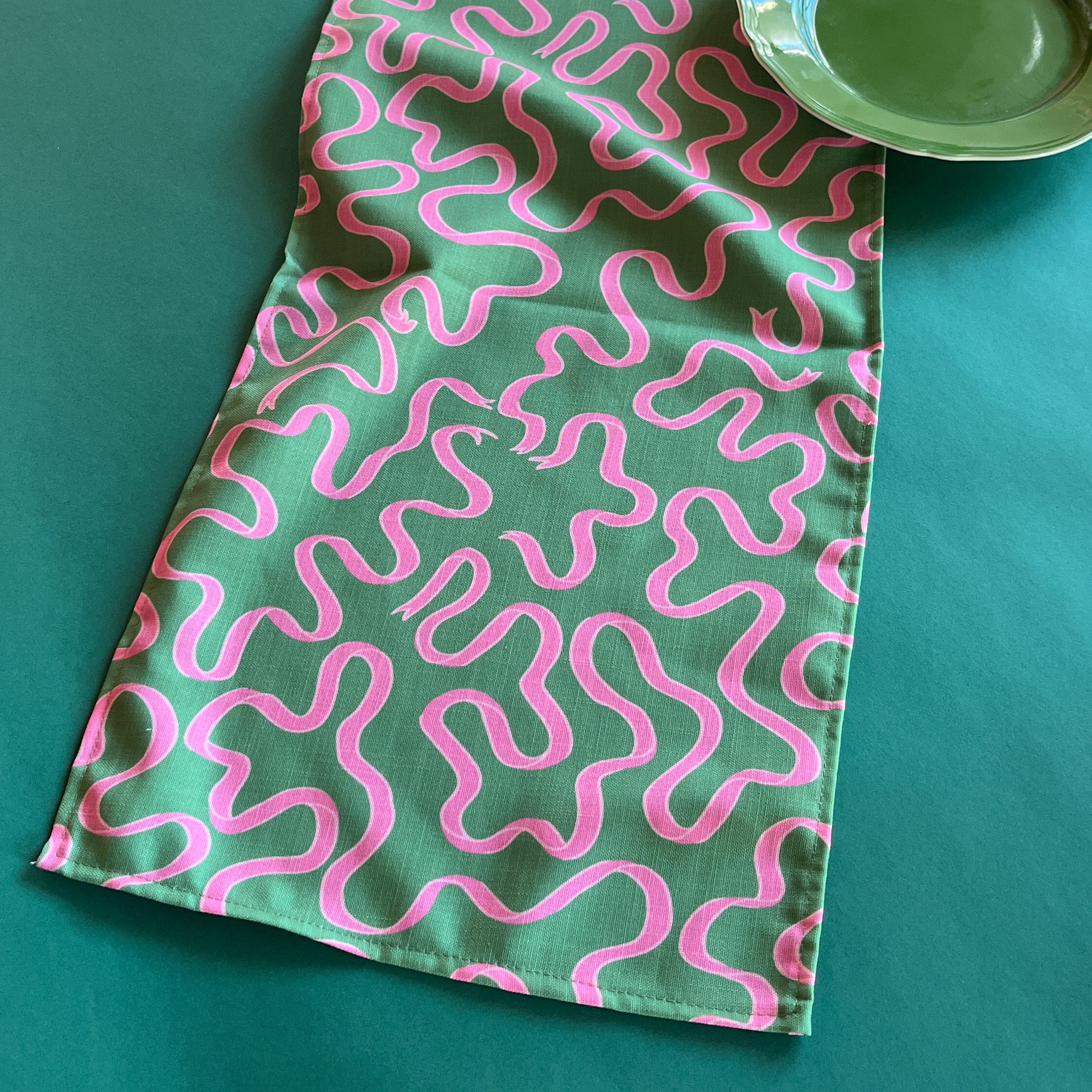 Pink ribbons swirl around on a green background in Madcap Cottage's Ribbons Pink and Green cloth table runner
