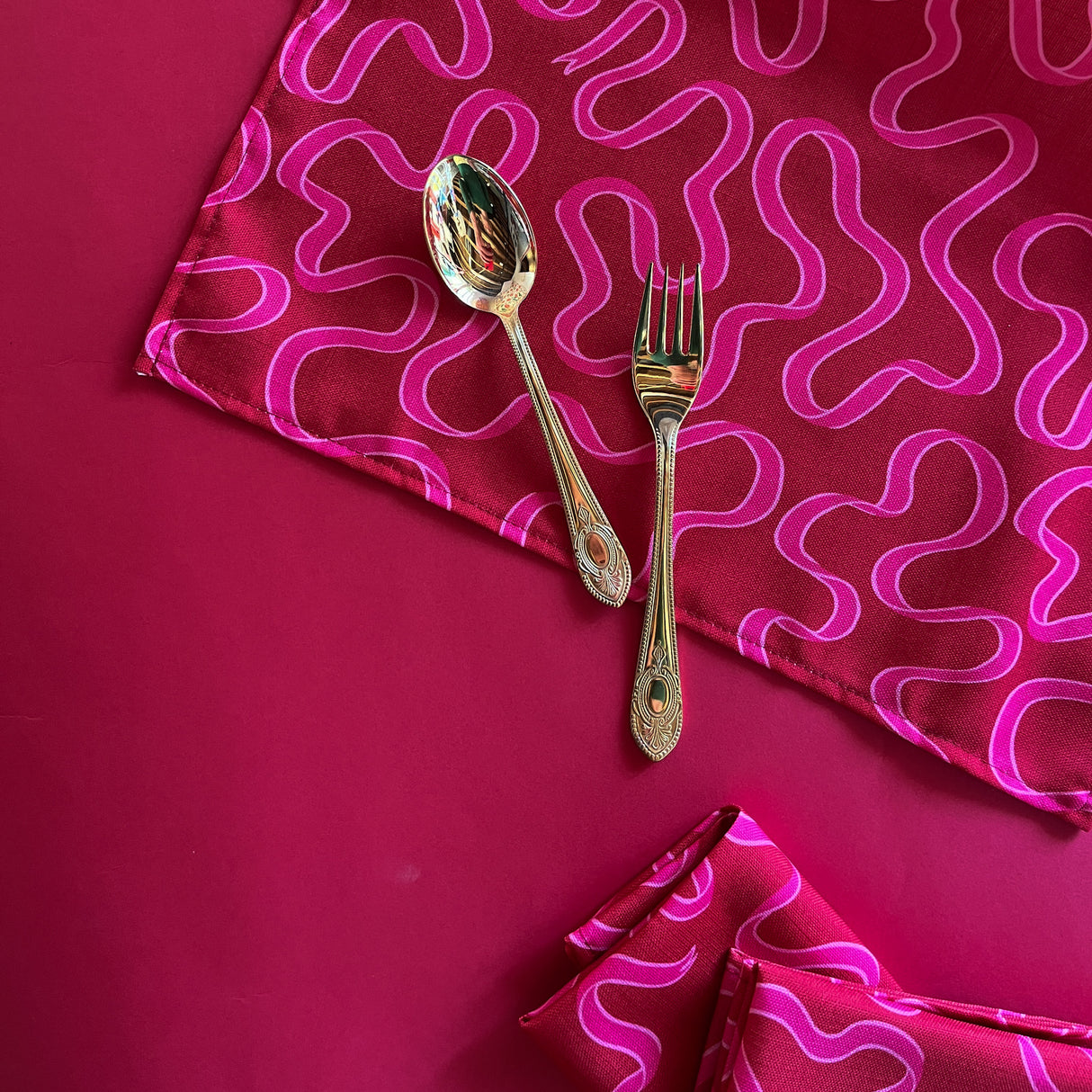 Corner of the Ribbons patterned red cloth dinner napkin with gold silverware resting on the napkin