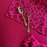 Corner of the Ribbons patterned red cloth dinner napkin with gold silverware resting on the napkin