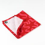 Red cotton napkin with pink wavy snake-inspired pattern, folded to show stitched edges and inner white lining.