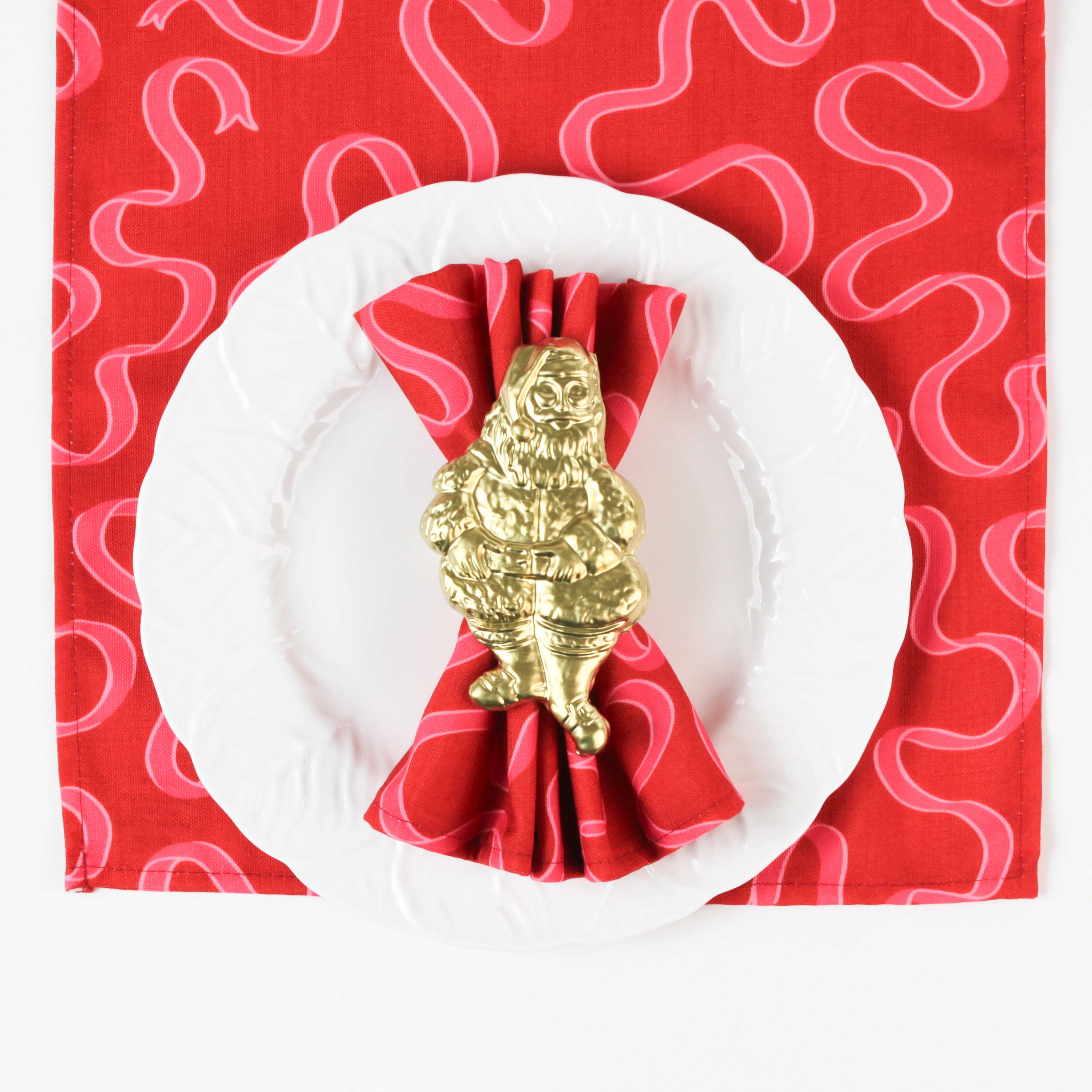 Red swirl-pattern Christmas napkin displayed on a white plate with a gold Santa napkin ring, festive holiday table décor.